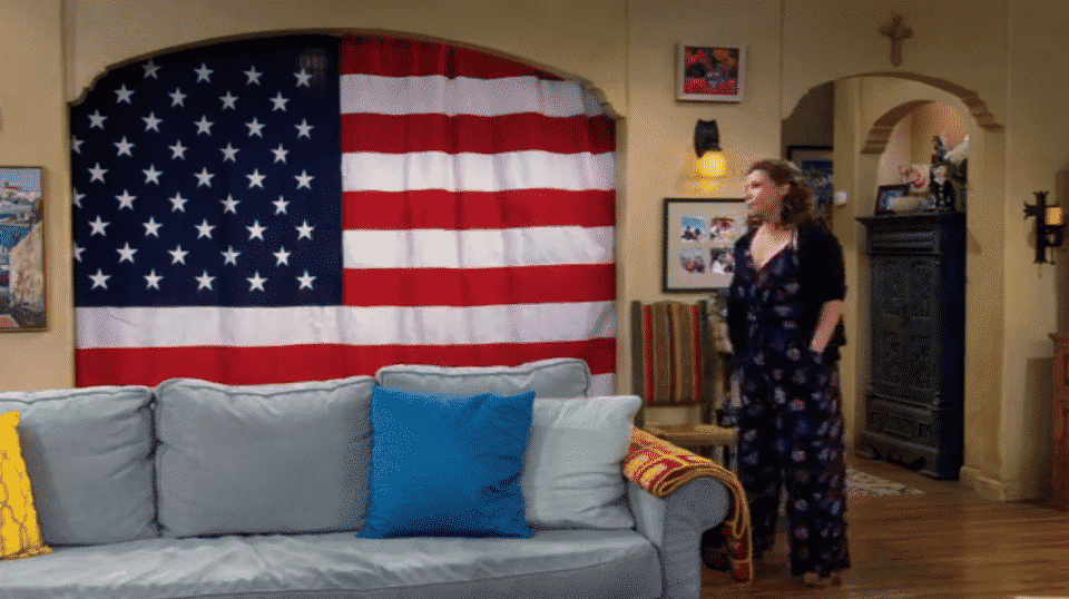 Penelope standing in front of Lydia's new curtains, which are the American flag.