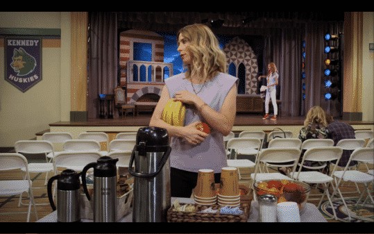 Jennifer taking a lot of fruit from a snack table.