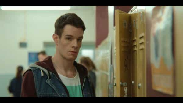 Adam (Connor Swindells) standing by a locker.