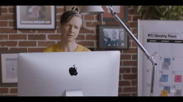 Gabe (John Cameron Mitchell) looking over his Mac computer towards Annie.