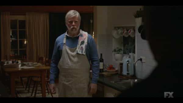 Dennis Miller (Paul Caesar) standing in his kitchen.