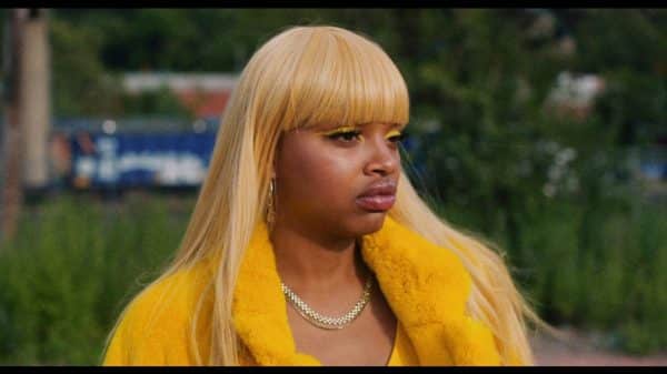 Goldie (Slick Woods) in a blonde wig and yellow mink coat.