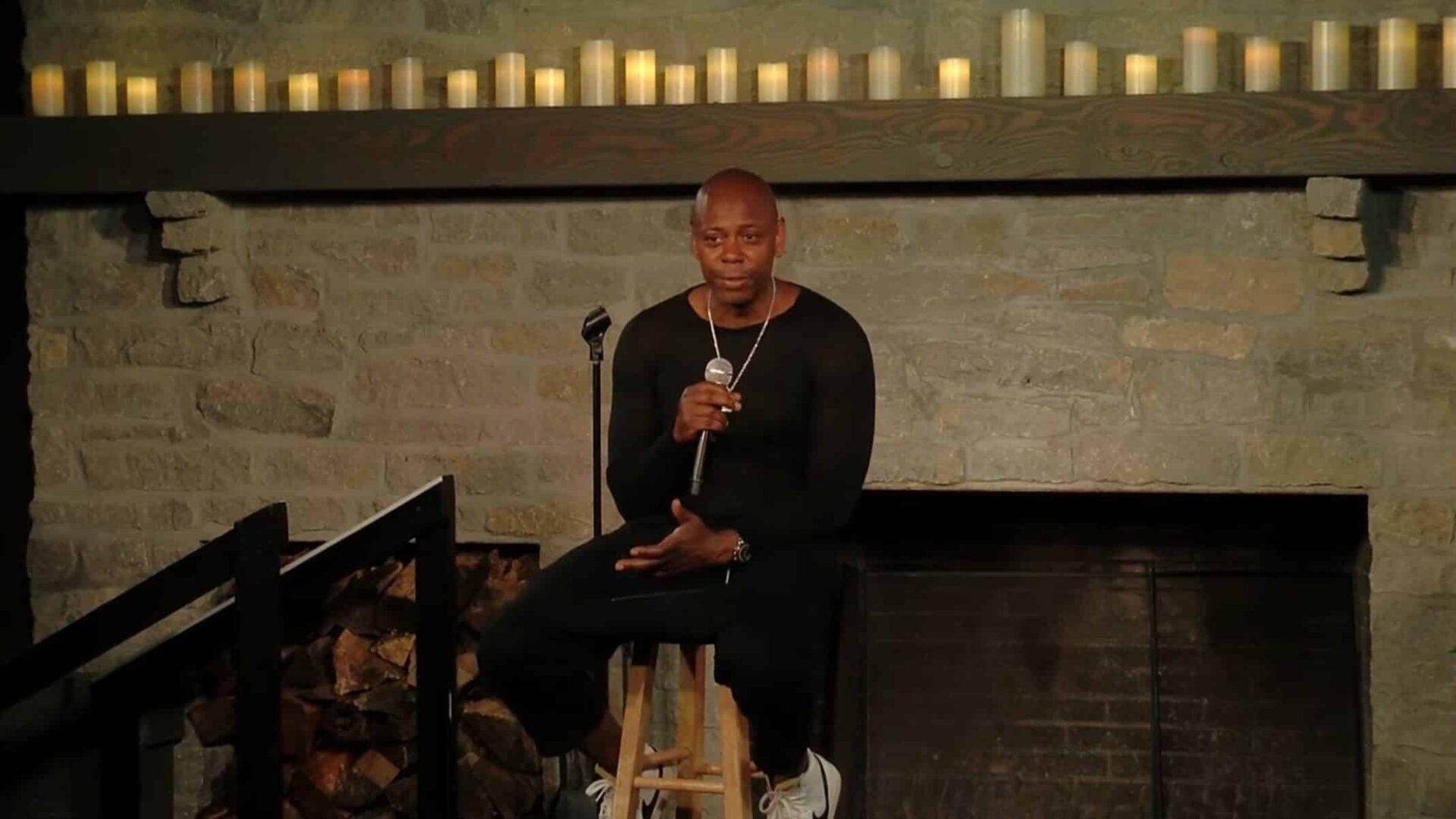 Dave Chappelle sitting on a stool, talking to an audience.