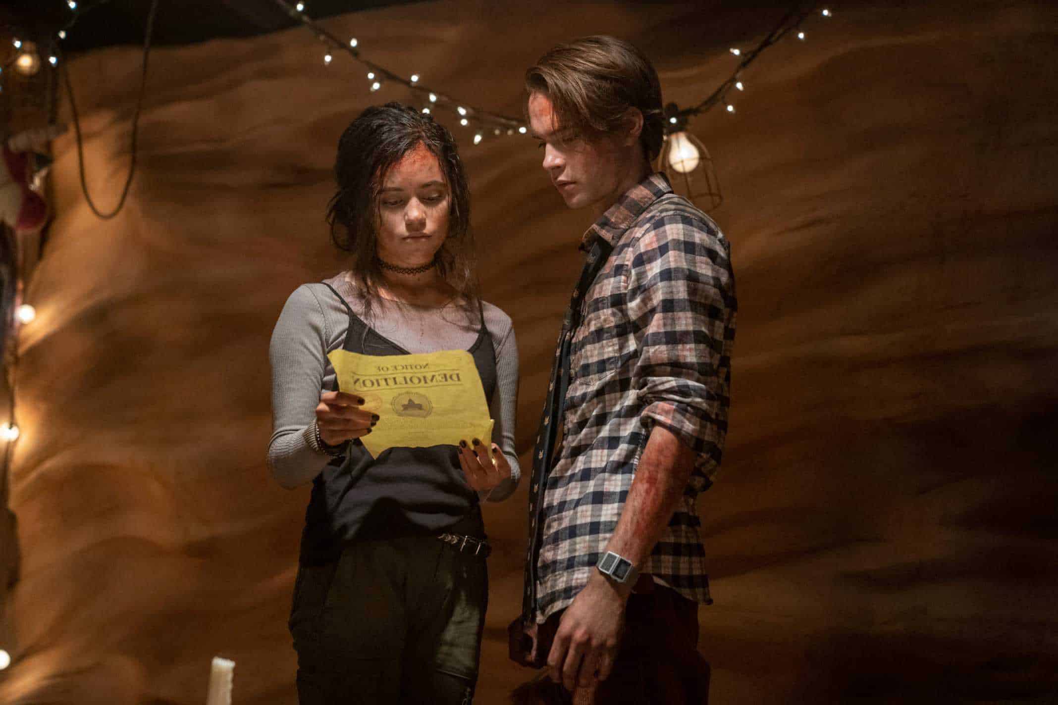 JENNA ORTEGA as PHOEBE and JUDAH LEWIS as COLE looking at a piece of paper, seemingly with blood on them.