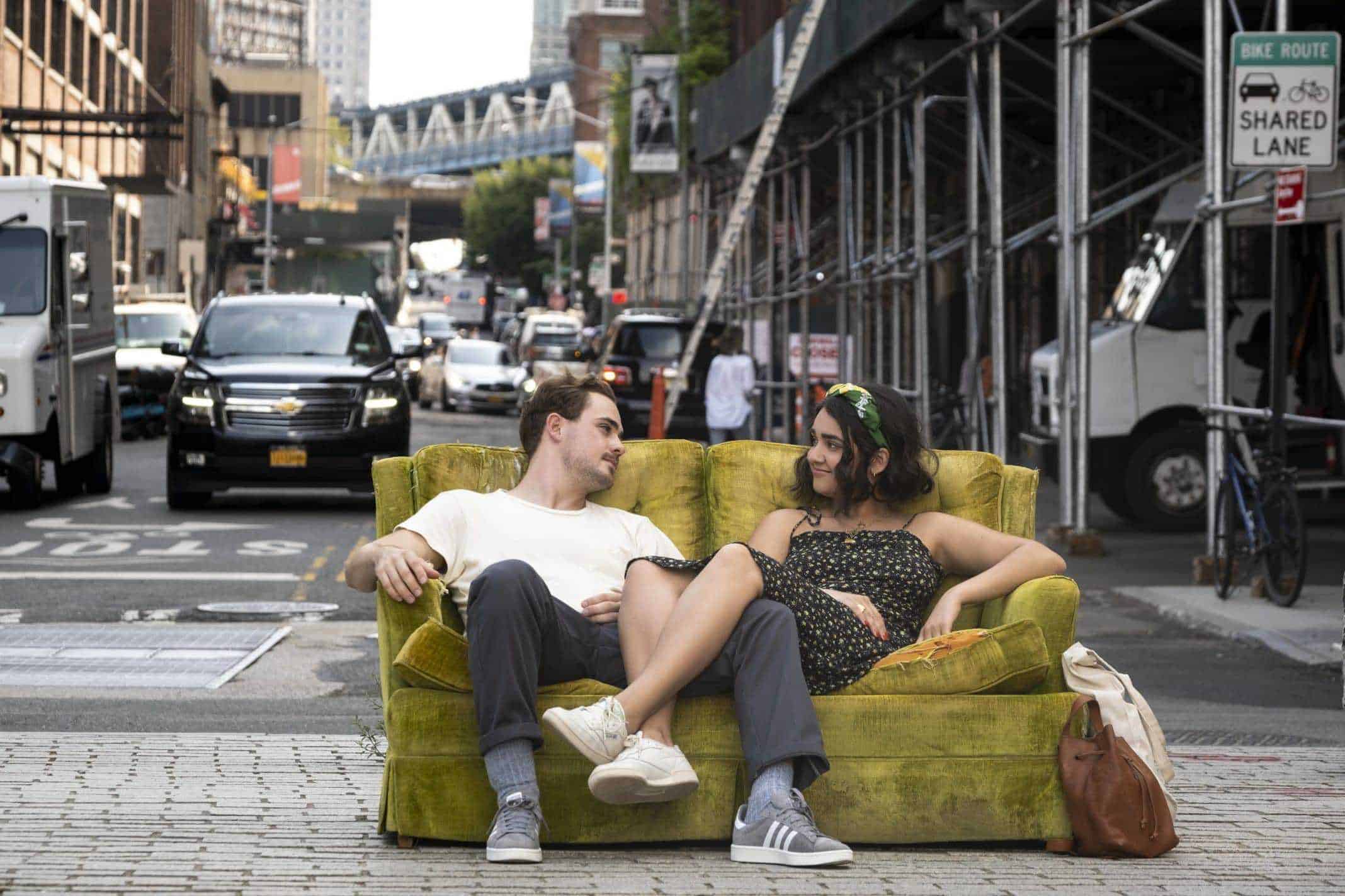 Nick (Dacre Montgomery) and Lucy (Geraldine Viswanathan) sitting on a couch together, outside.