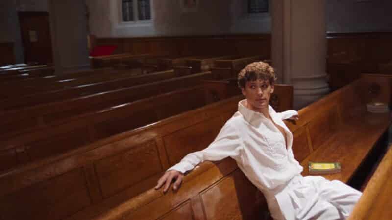 Azrael (Cooper Koch) sitting in a pew.