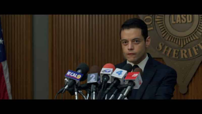 Jim (Rami Malek) holding a press conference