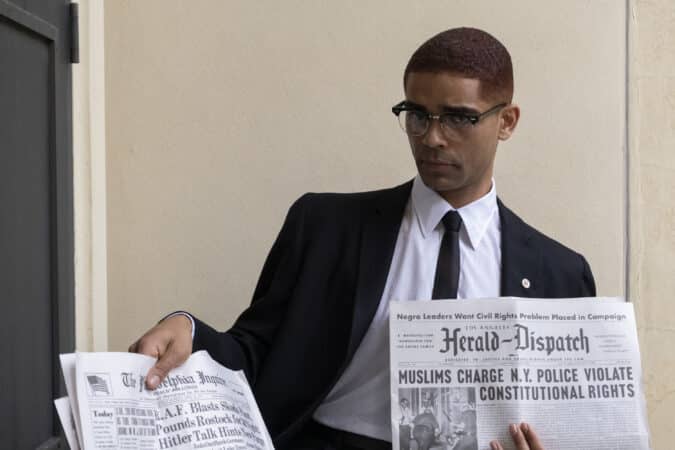 Malcolm X (Kingsley Ben-Adir) holding up a newspaper