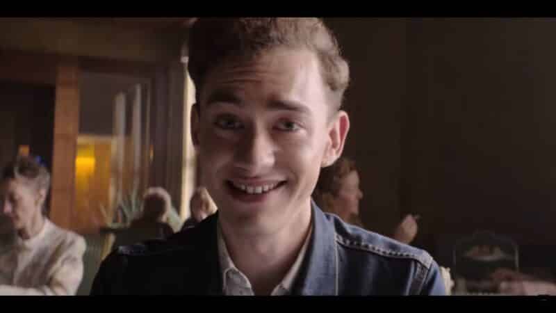 Ritchie (Olly Alexander) smiling and talking to a potential agent