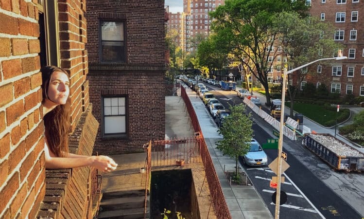 Mae (Marianne Rendon) leaning out her window