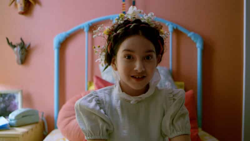 Ceci (Blanca Ordaz) in a wildflower crown, sitting on her bed.