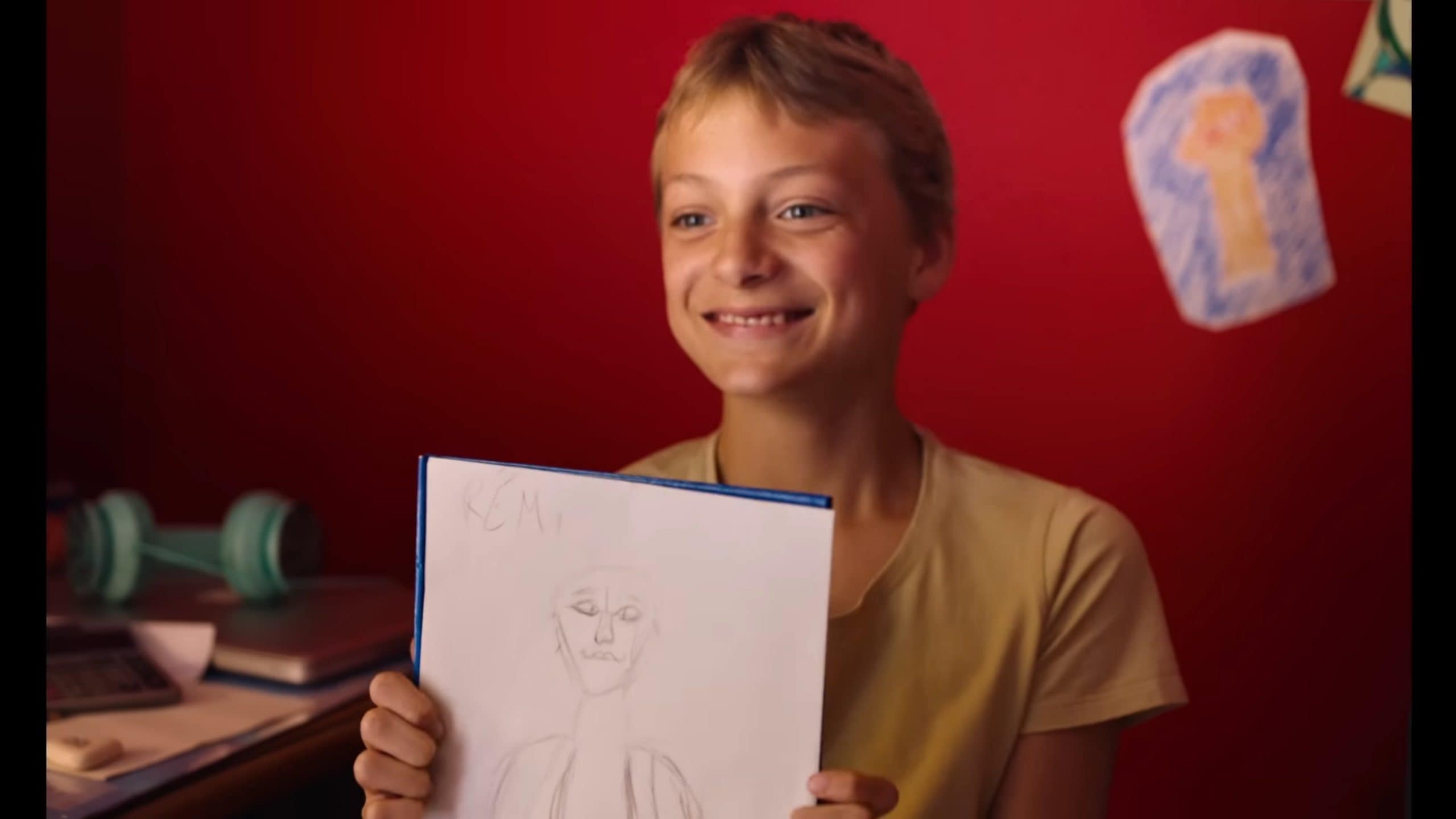 Leo (Eden Dambrine) smiling and showing Remi a picture he drew of him