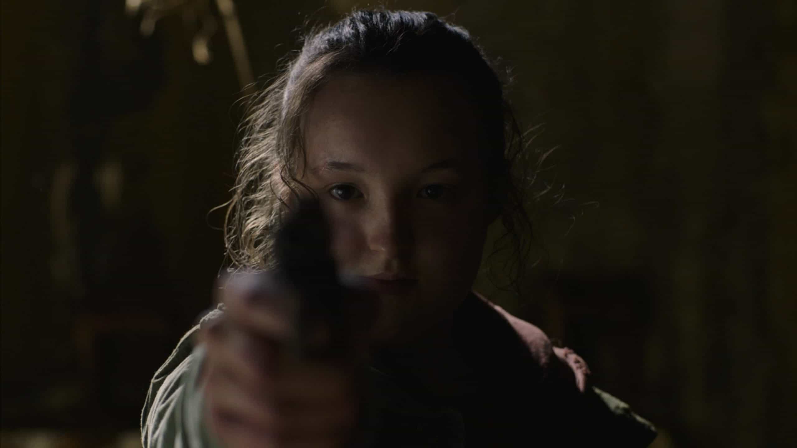 Bella Ramsey as Ellie holding a gun towards a mirror