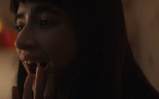 Sasha (Sara Motpetit) checking her teeth that have come in, Humanist Vampire Seeking Consenting Suicidal Person, directed by Ariane Louis-Seize, 2024, (Drafthouse Films)