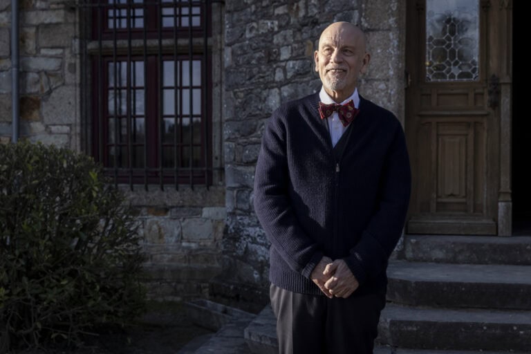 Andrew Blake (John Malkovich) standing in front of the Beauvillier estate – Mr. Blake At Your Service